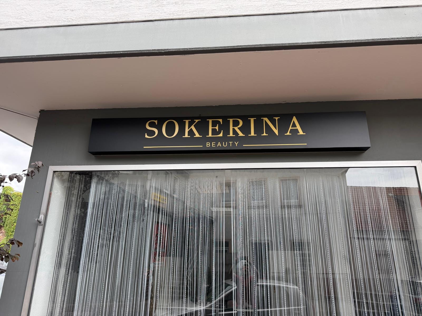 Schwarzes Ladenschild mit goldenem Schriftzug Sokerina Beauty über dem Schaufenster