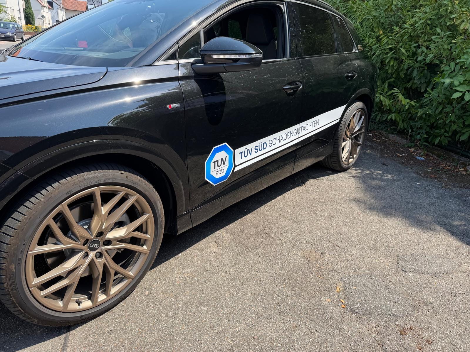 Schwarzer Audi mit weißem Seitenstreifen, Schriftzug TÜV SÜD Schadengutachten und TÜV-SÜD-Logo an der Fahrertür